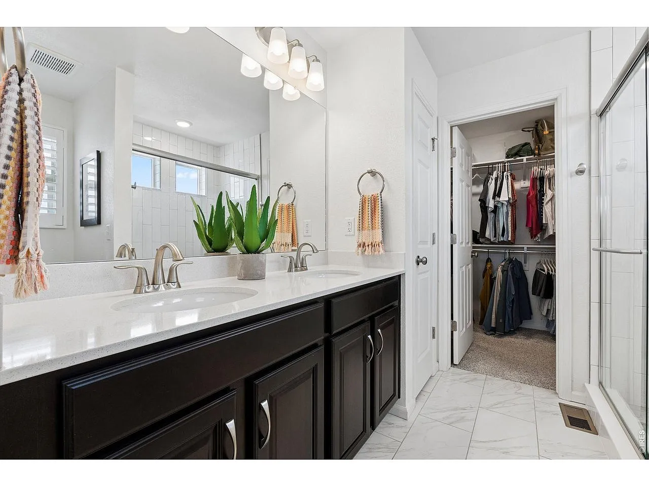 Primary bathroom with quartz double vanity and walk-in closet beyond