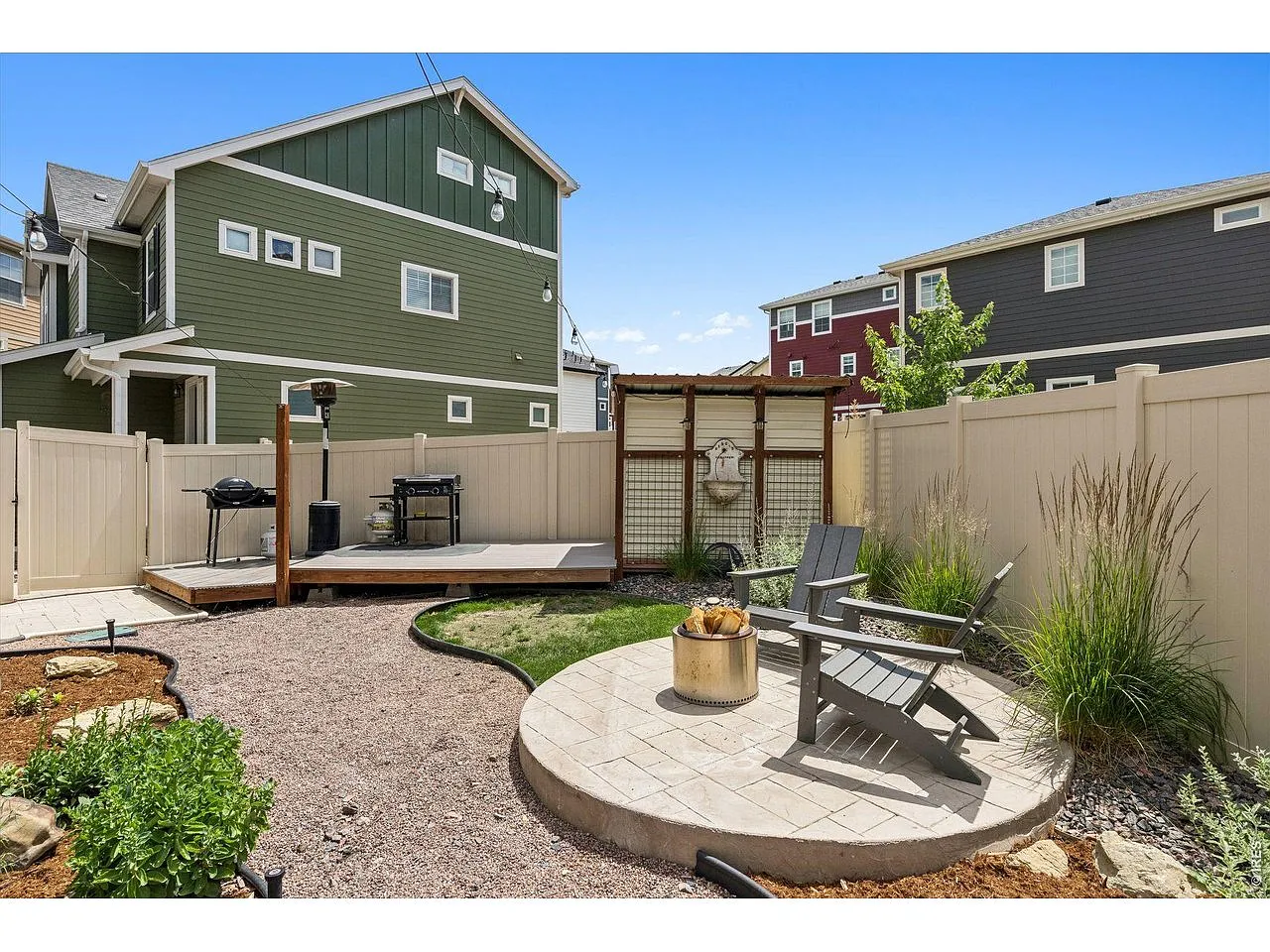 Fenced backyard with a paver fire-pit circle, Adirondack chairs and grill deck